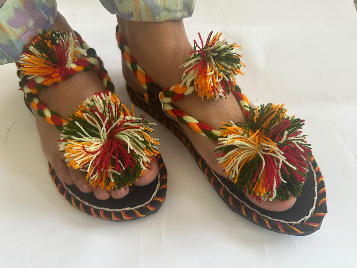 Pair of multicolour pom pom Balochi chappals worn by a woman – front view