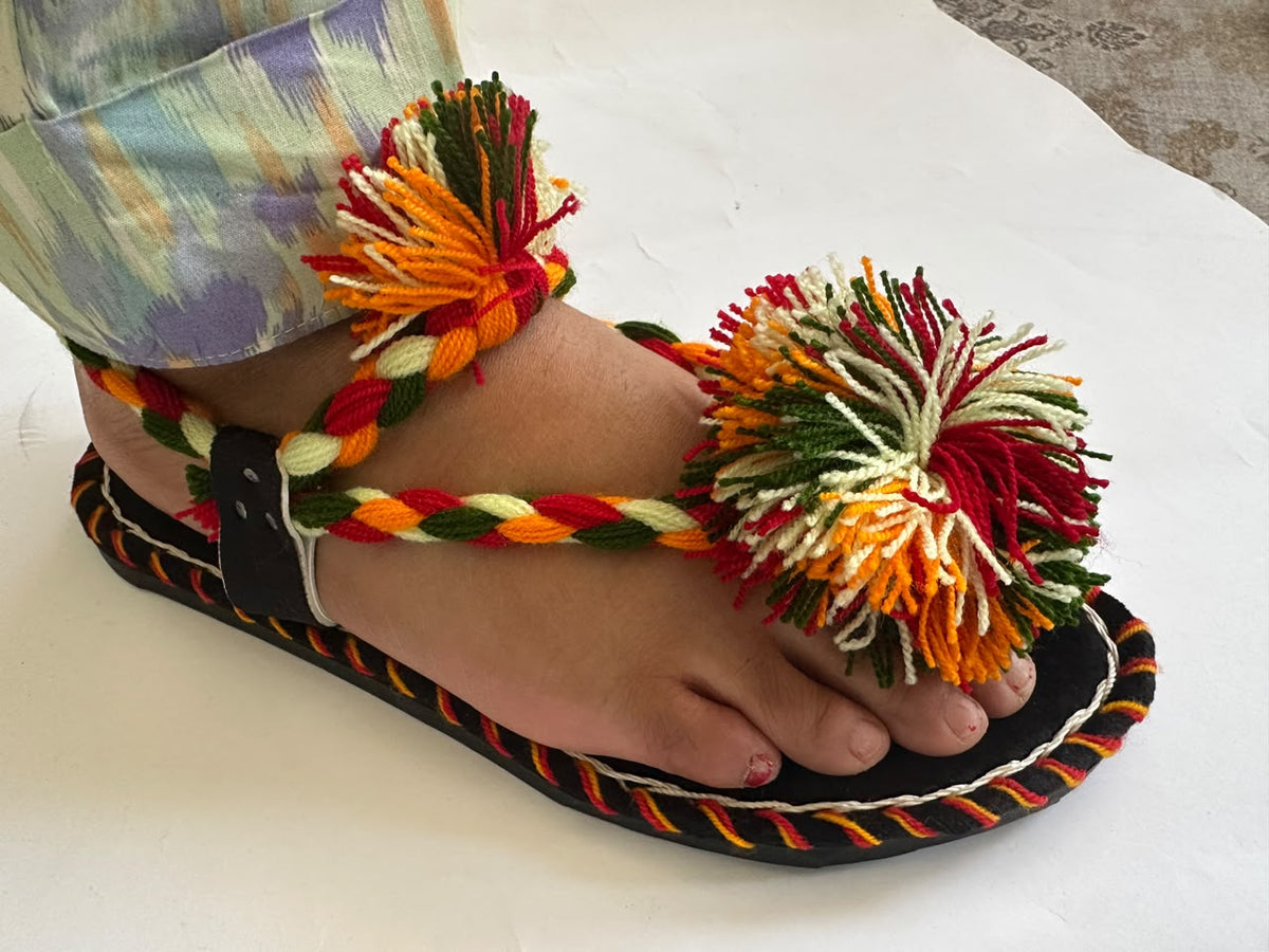 Woman wearing a handmade Balochi chawat chappal with multicolour pom poms and braided straps – side view